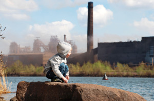 Plaing little boy on the river coast in front of metallurgy plant